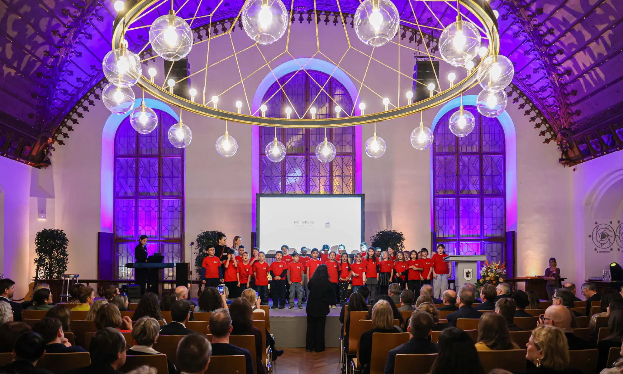 Blick auf die Kinder des Superar Chors auf der Bühne, Publikum und Leuchter sind zu sehen.